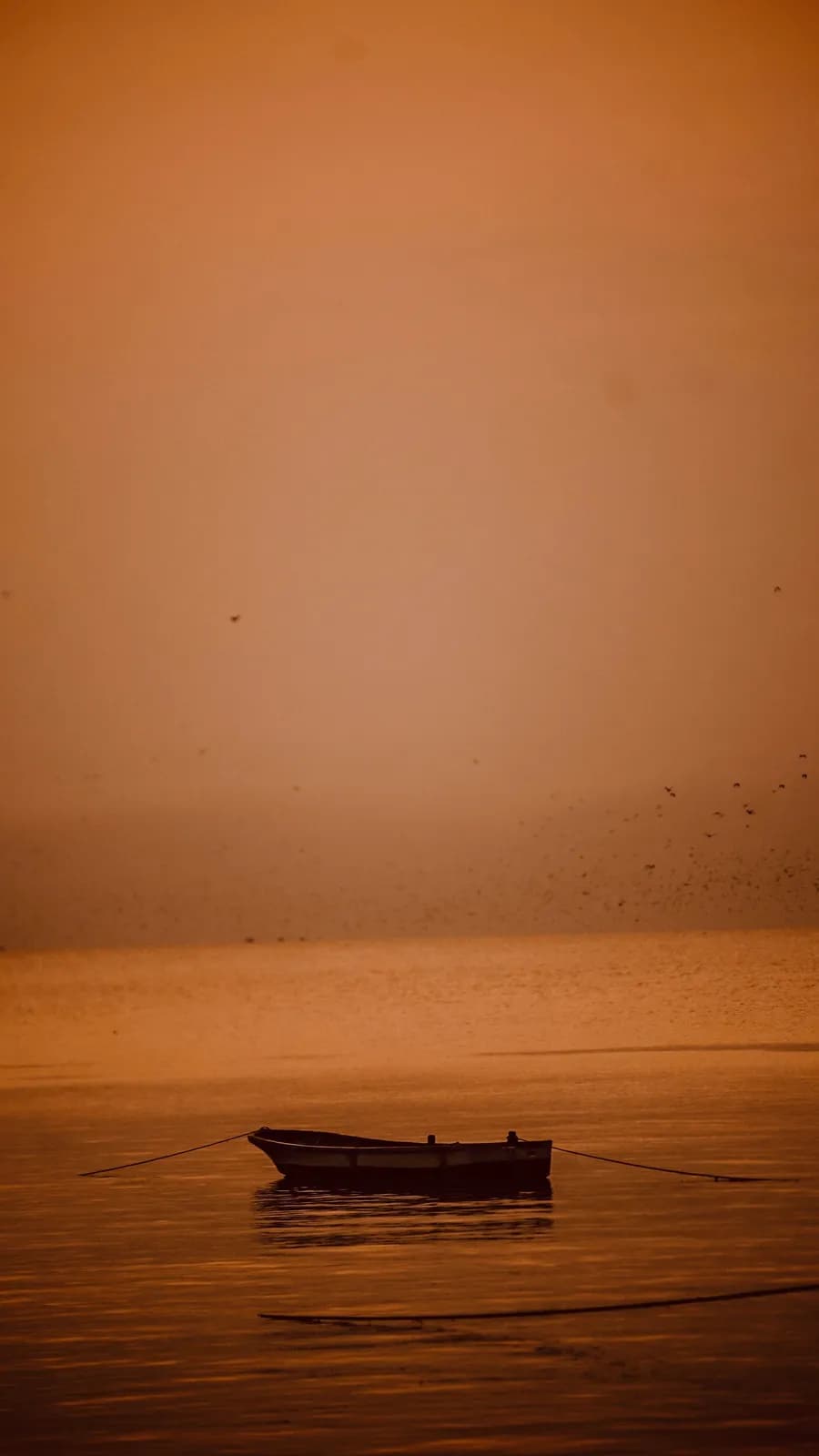 Small fishing boat floating on calm water during a peaceful golden sunset at the horizon