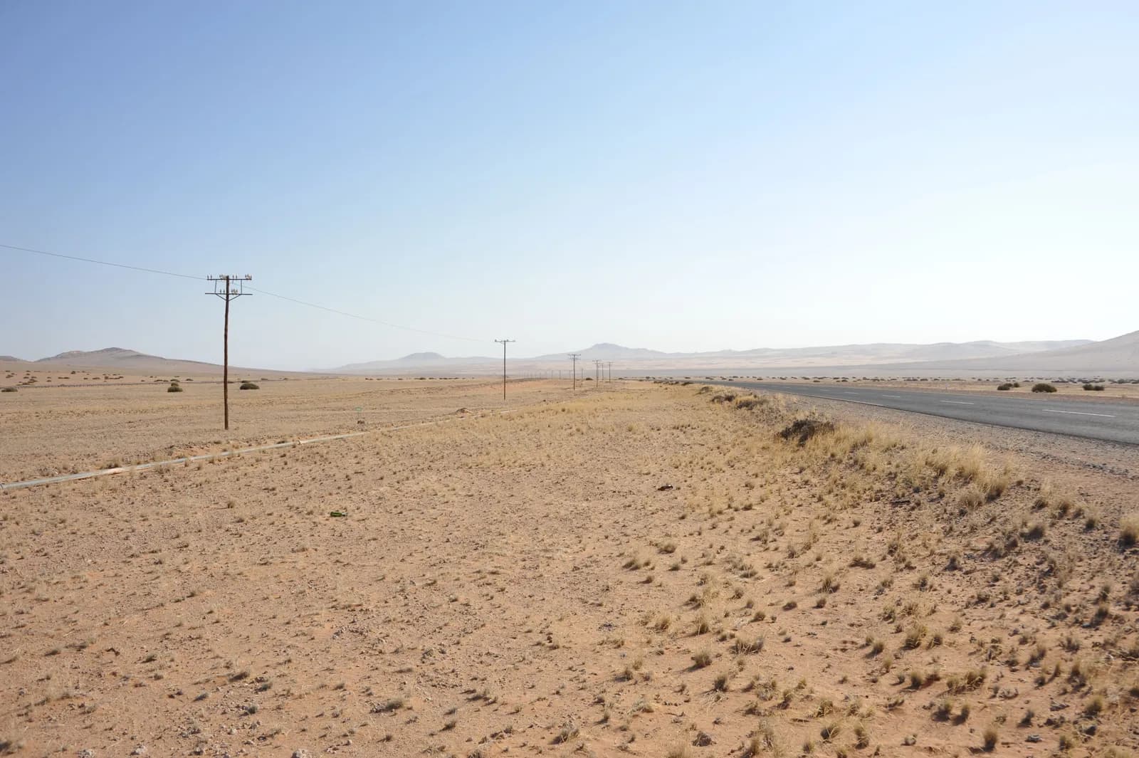 Asphalt road stretching through a vast arid desert landscape under a clear blue sky