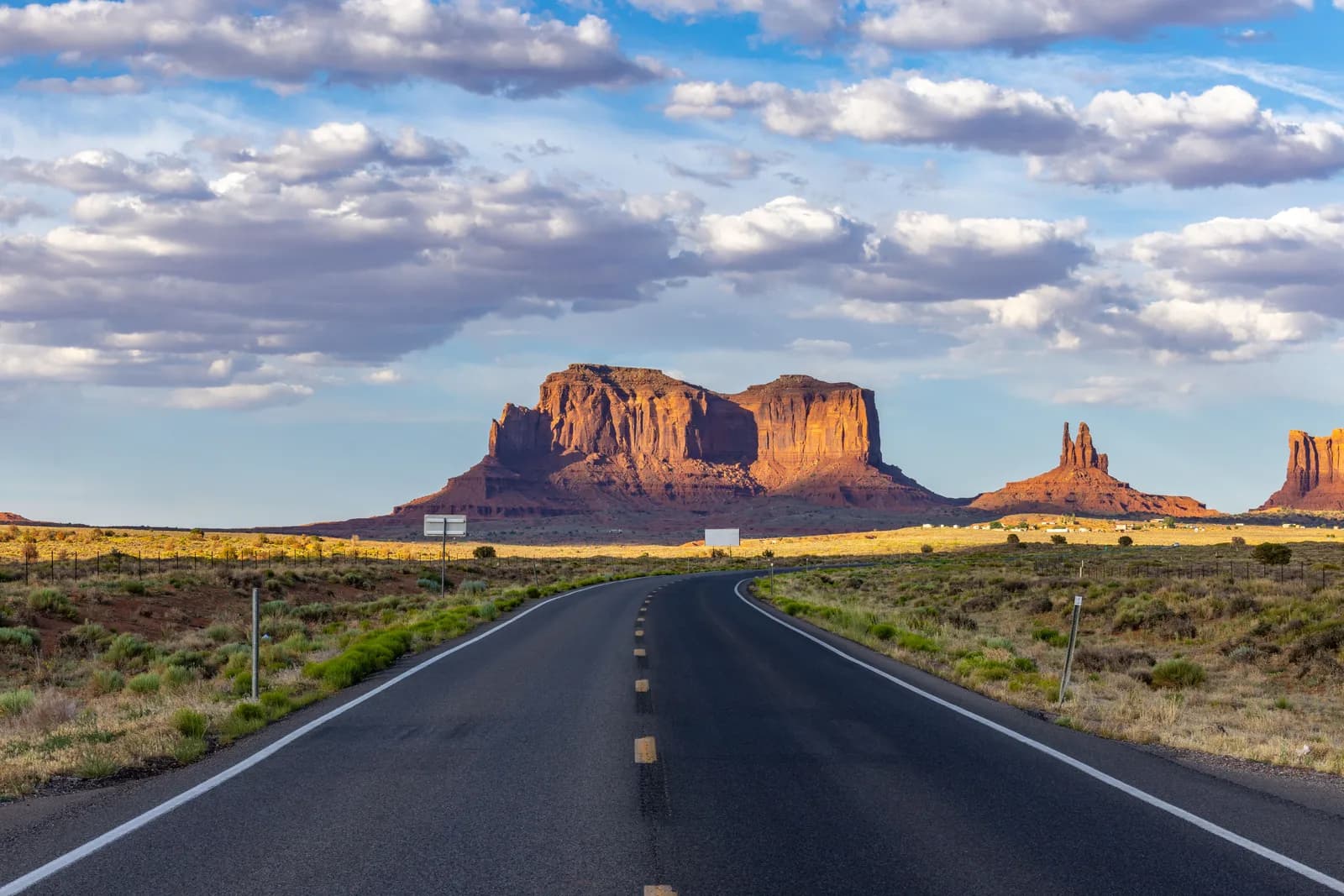 Scenic asphalt road leading to monument valley buttes under a cloudy blue sky at sunset