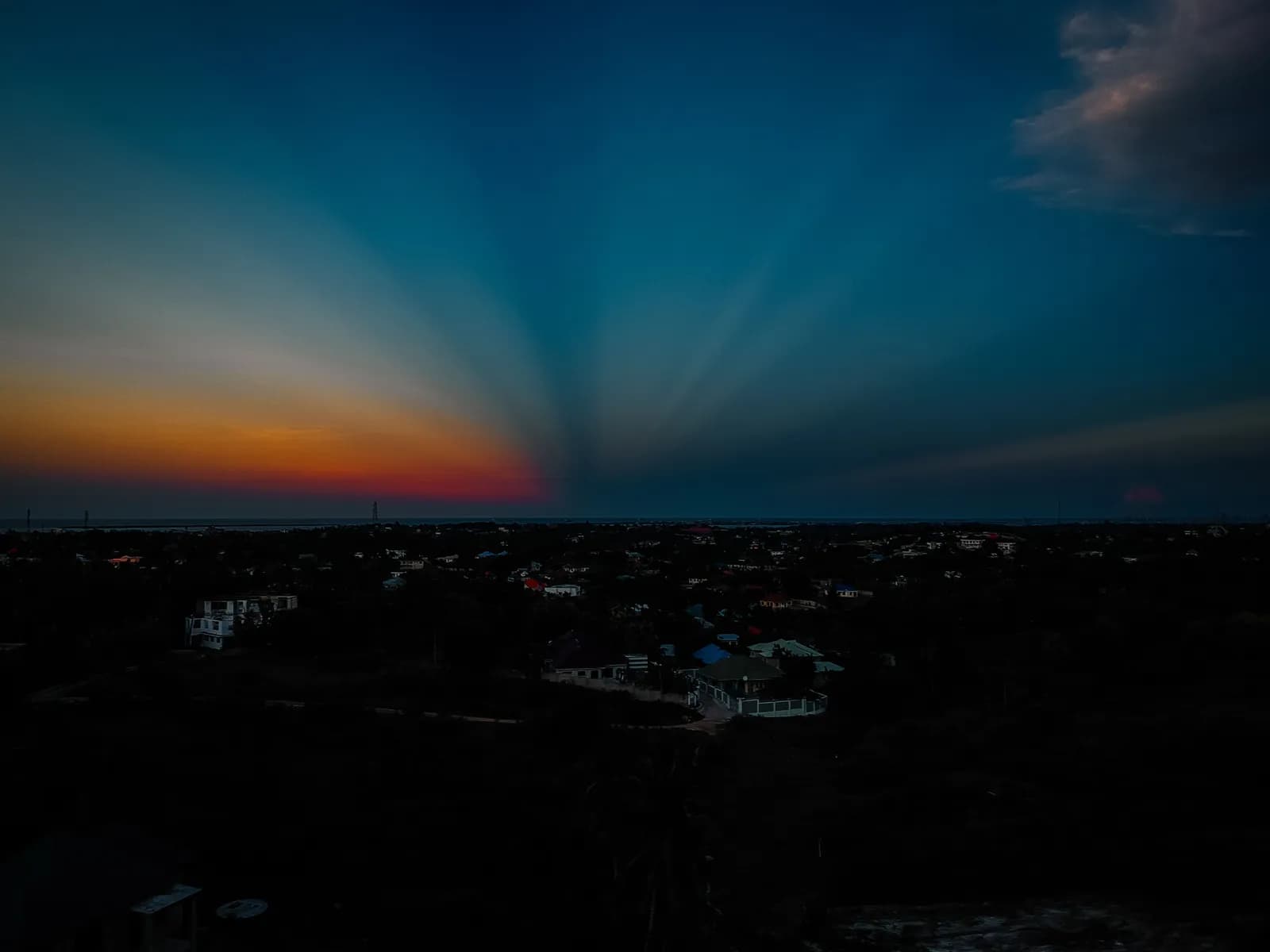 Dramatic sunset sky with crepuscular rays over a dark suburban landscape at twilight hour