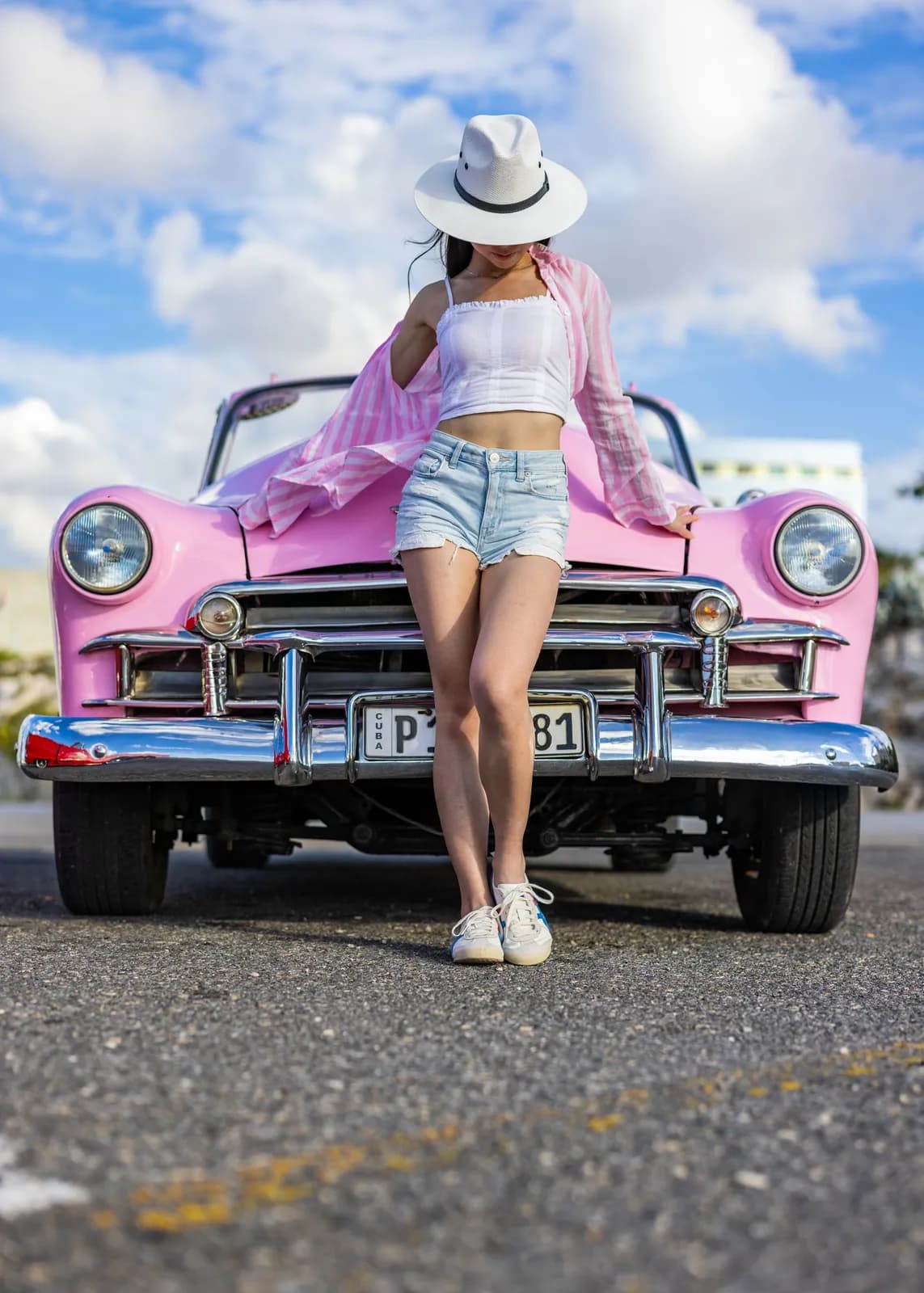 Young woman posing in front of a vintage pink convertible car on a sunny day