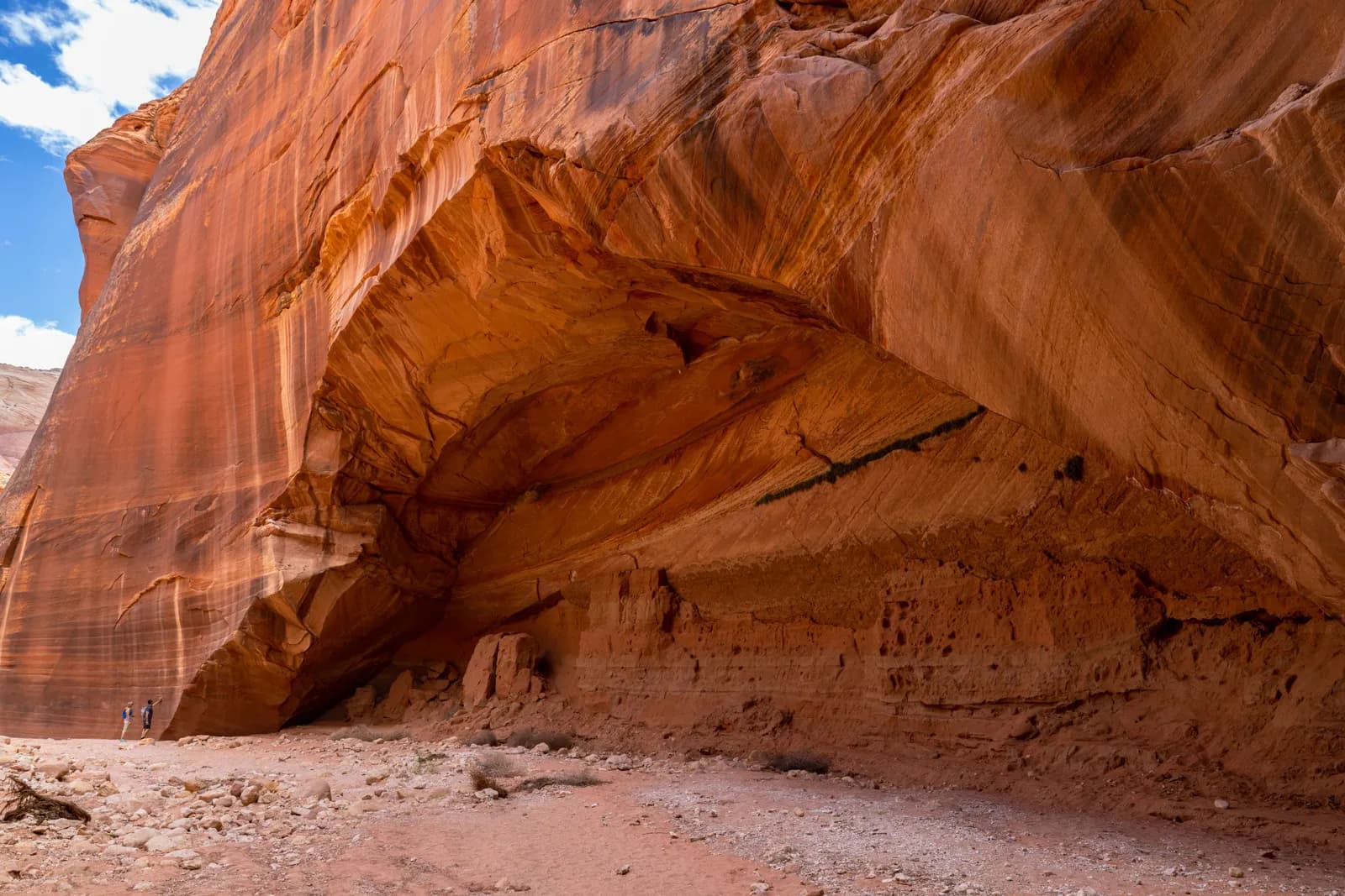 Massive red sandstone canyon alcove with hikers exploring desert landscape in utah wilderness area