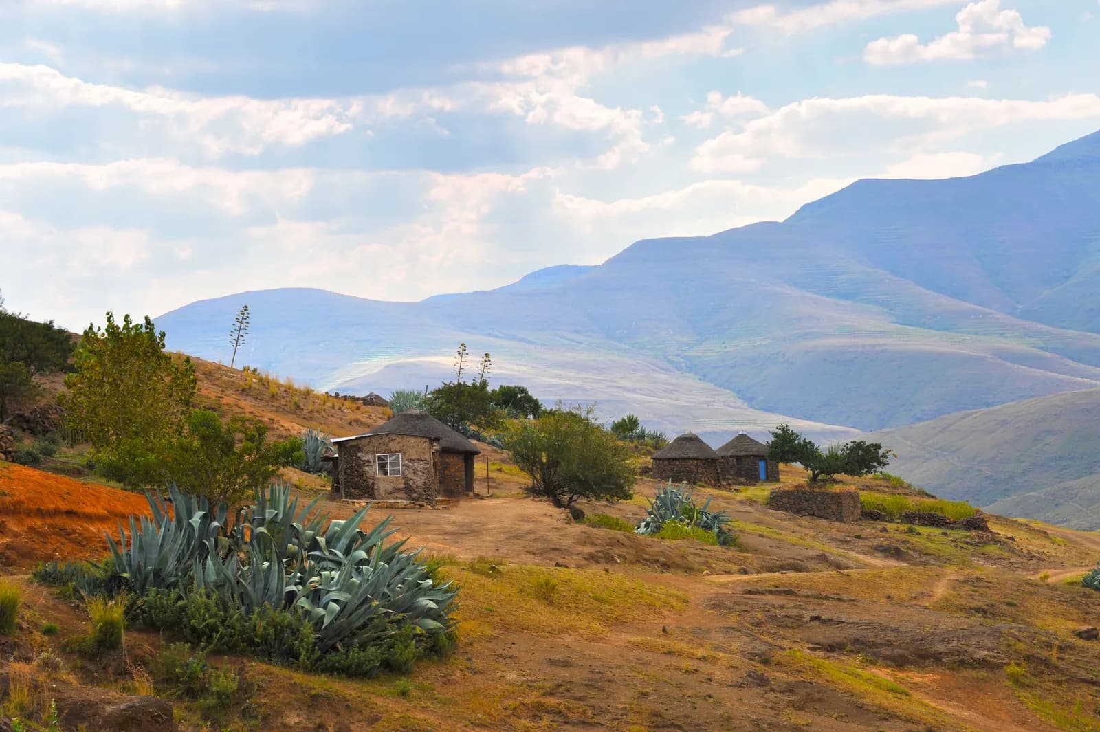 Traditional stone huts in a rural mountain landscape with agave plants and blue sky
