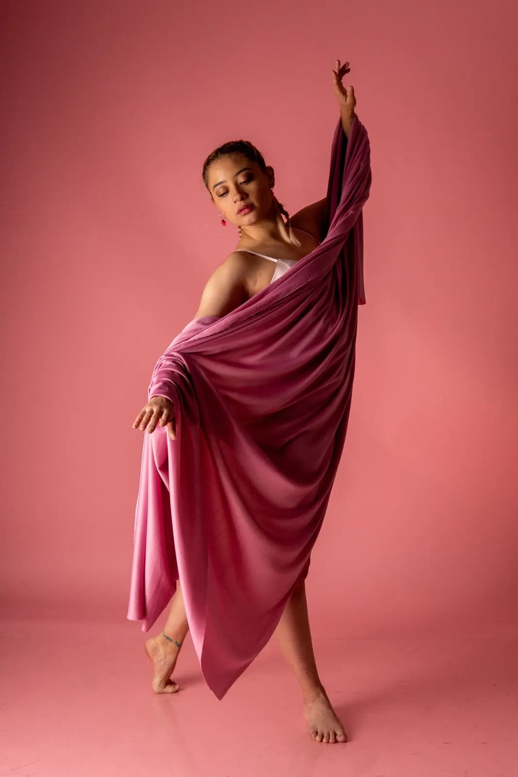 Graceful female dancer performing contemporary dance in flowing pink fabric against pink background
