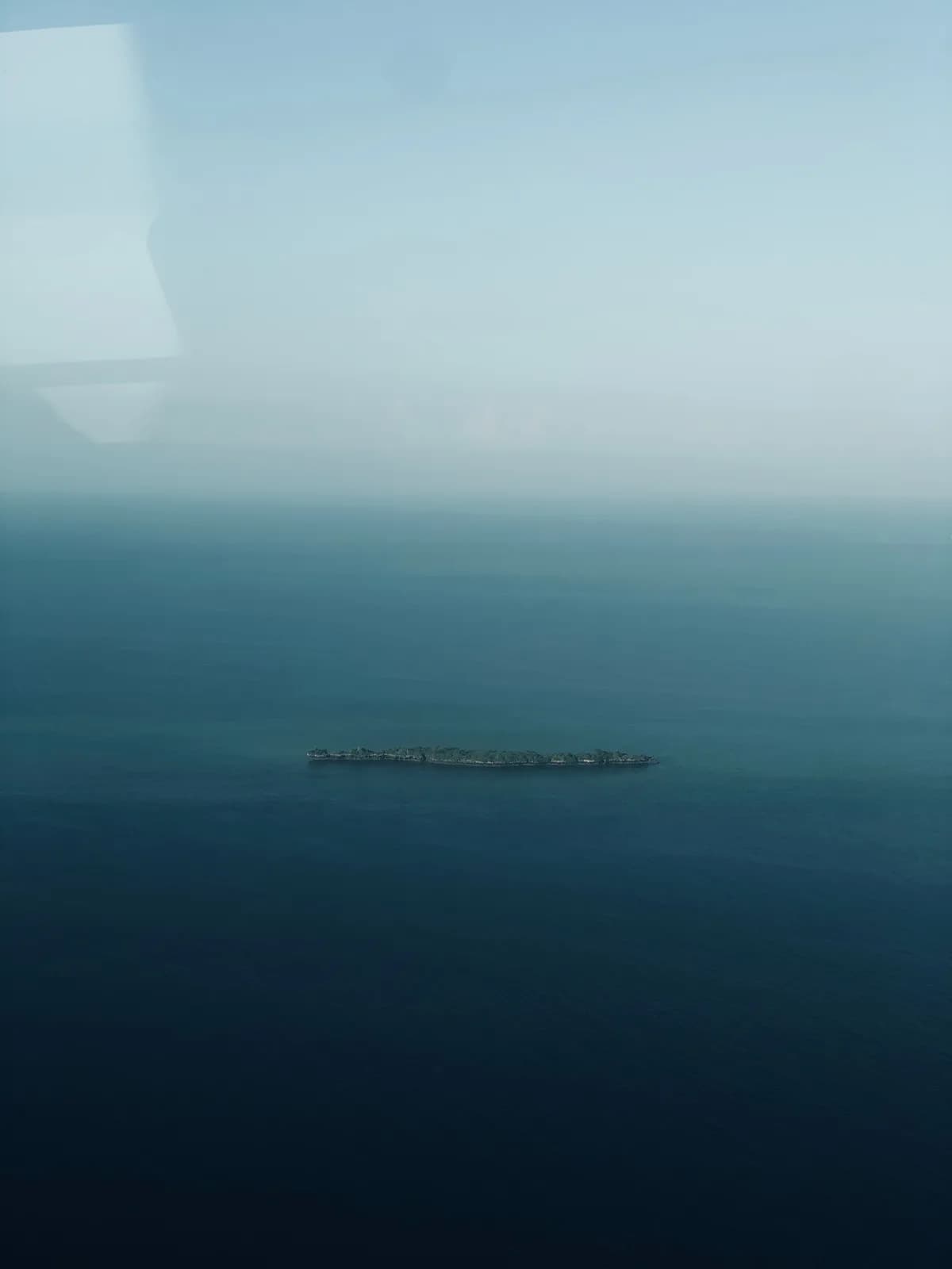 Aerial view of a small remote island surrounded by deep blue ocean water during a clear sunny day