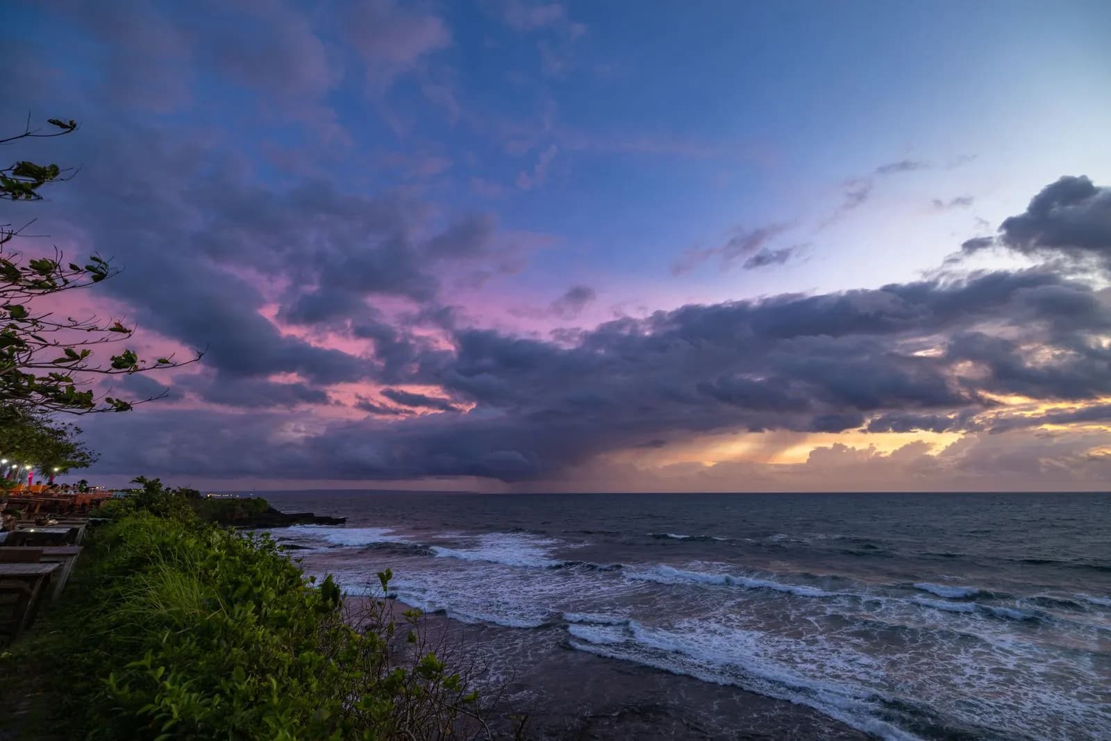 Dramatic sunset over tropical ocean waves crashing on rocky coastline at dusk