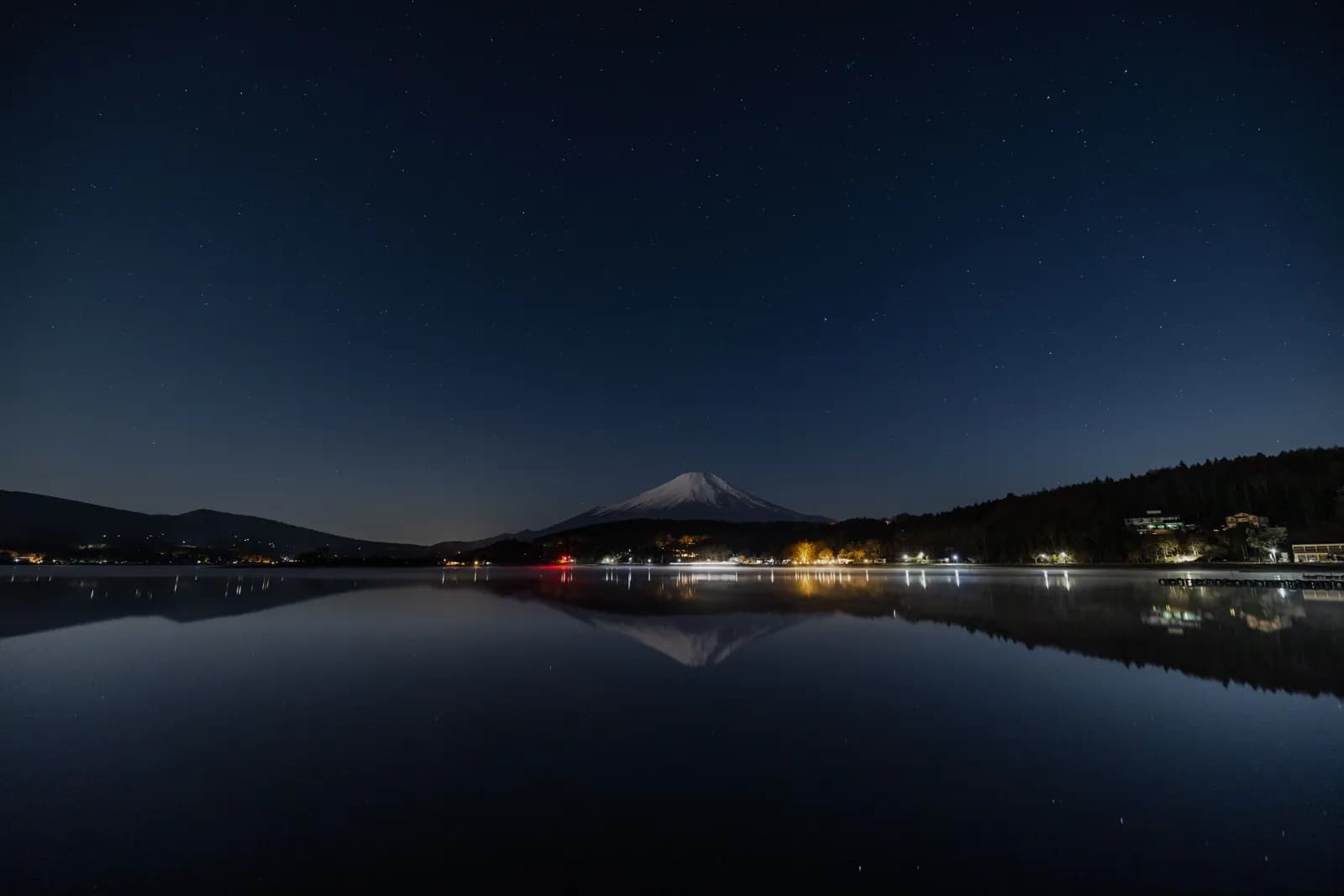 Mount fuji reflected in lake kawaguchi at night with starry sky and distant town lights in japan
