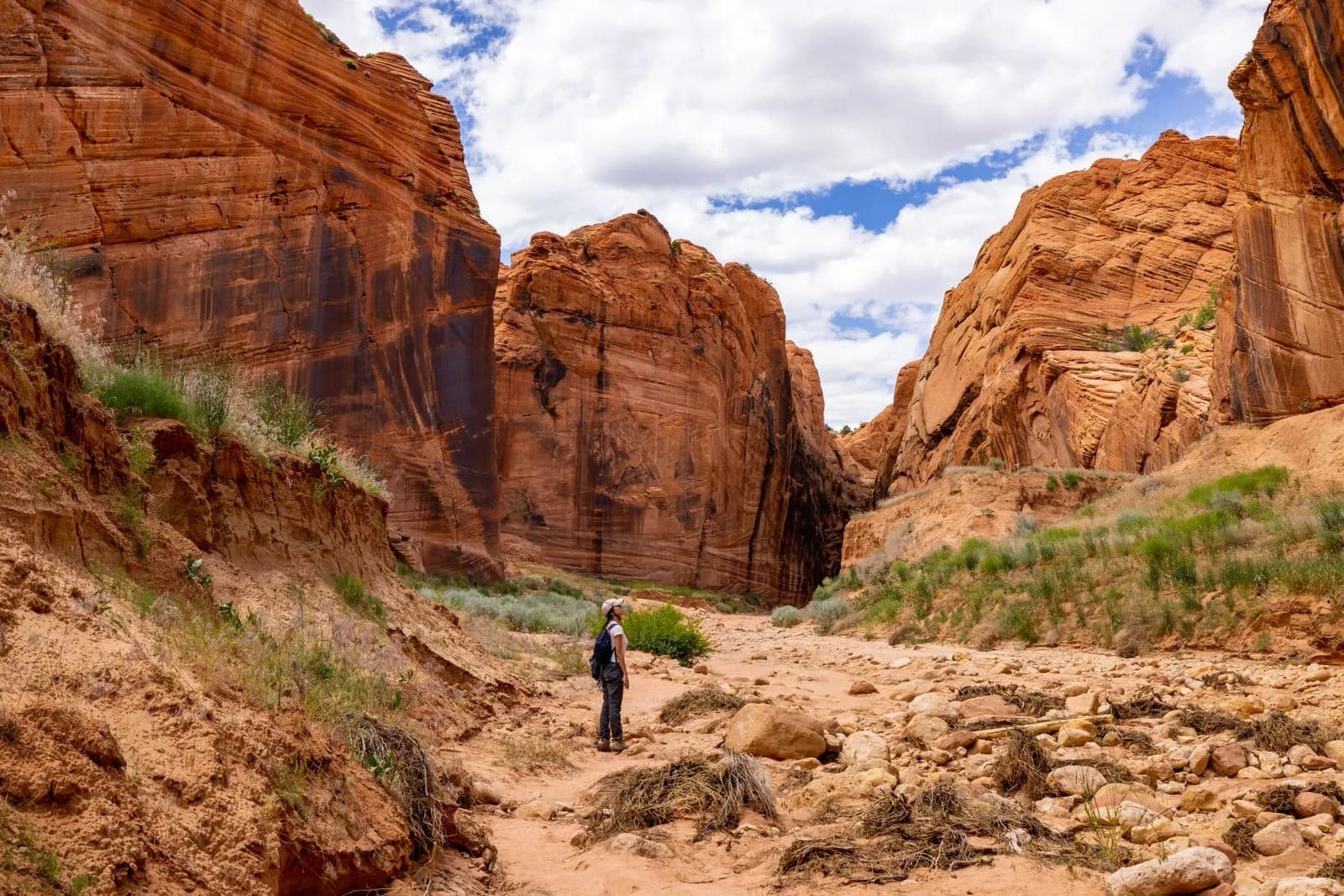 Hiker exploring a narrow desert canyon with towering red sandstone rock formations under blue sky