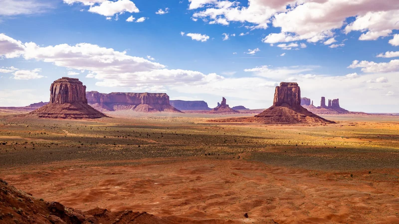 Scenic view of monument valley buttes under a bright blue sky with clouds in a desert landscape