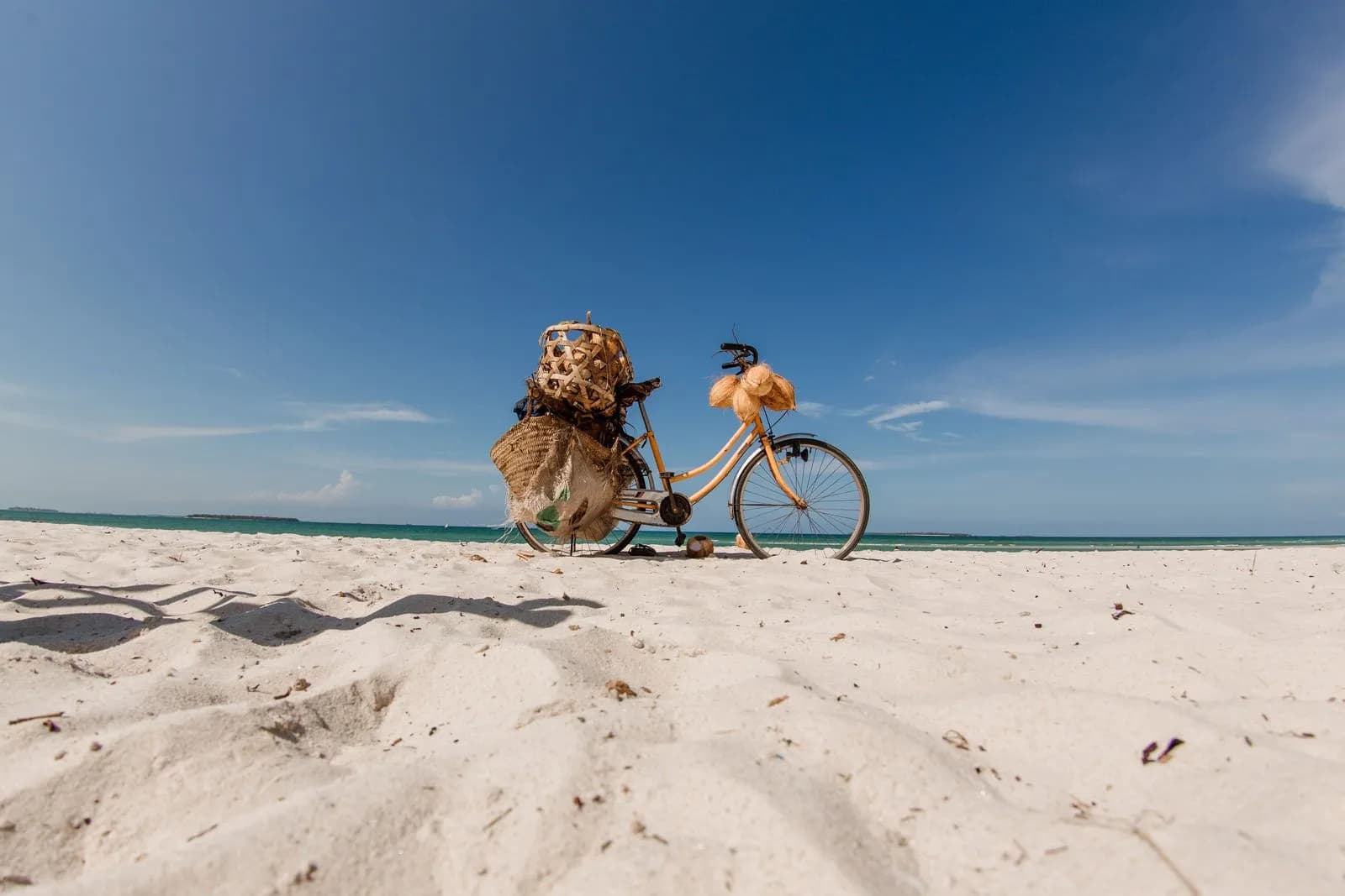 Vintage bicycle with woven baskets parked on a tropical white sand beach under clear blue sky