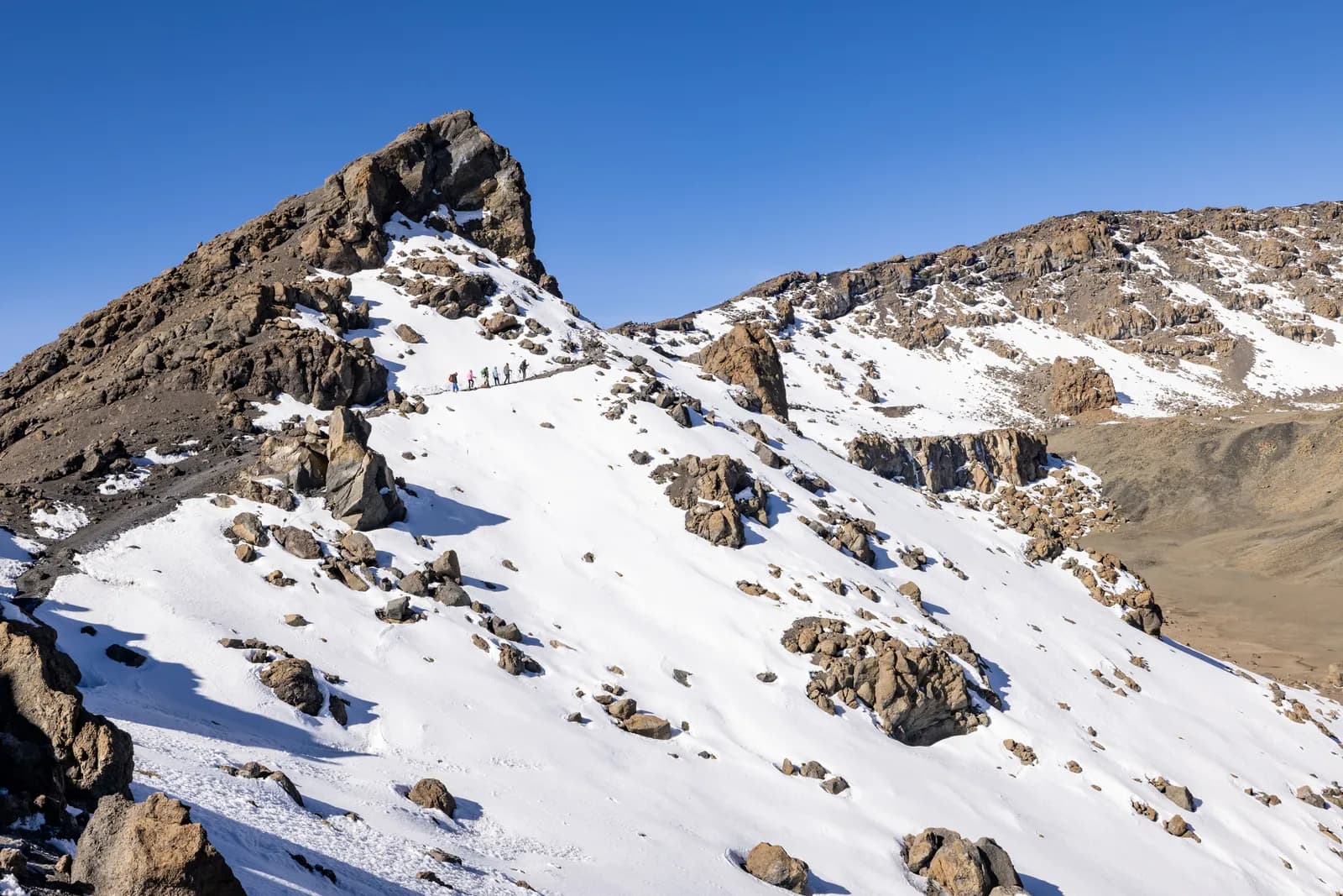 Group of hikers trekking up a steep snowy mountain slope during a sunny winter expedition adventure