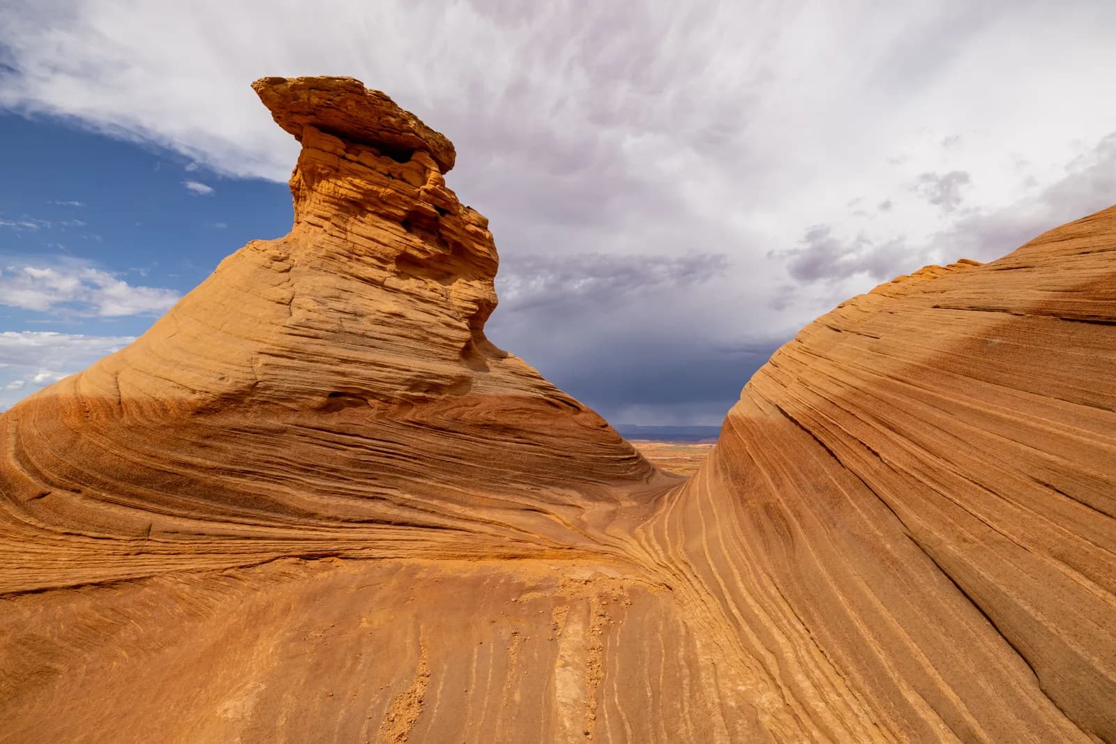 Scenic sandstone rock formation in a desert landscape under a dramatic cloudy sky at sunset