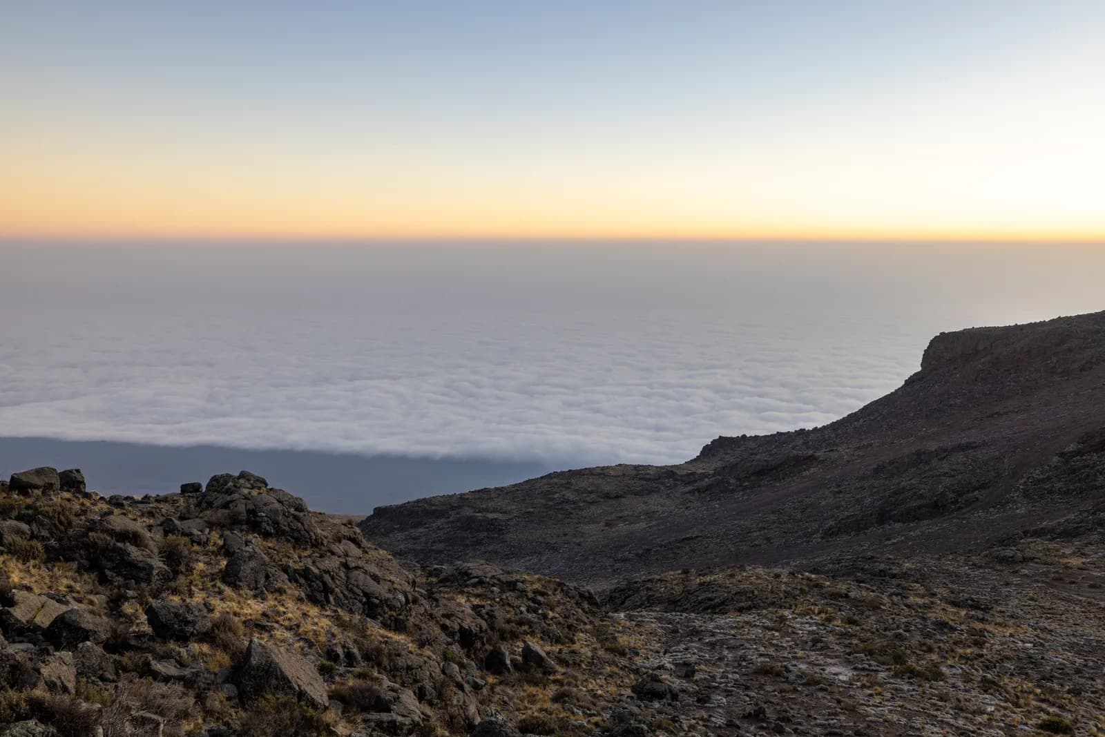 Panoramic view of mountain peak above clouds at sunrise with rocky terrain in foreground