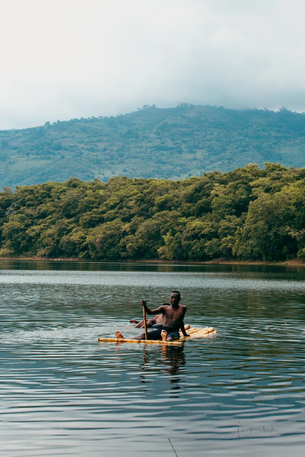 Man paddling traditional wooden canoe on serene tropical lake surrounded by lush green hills