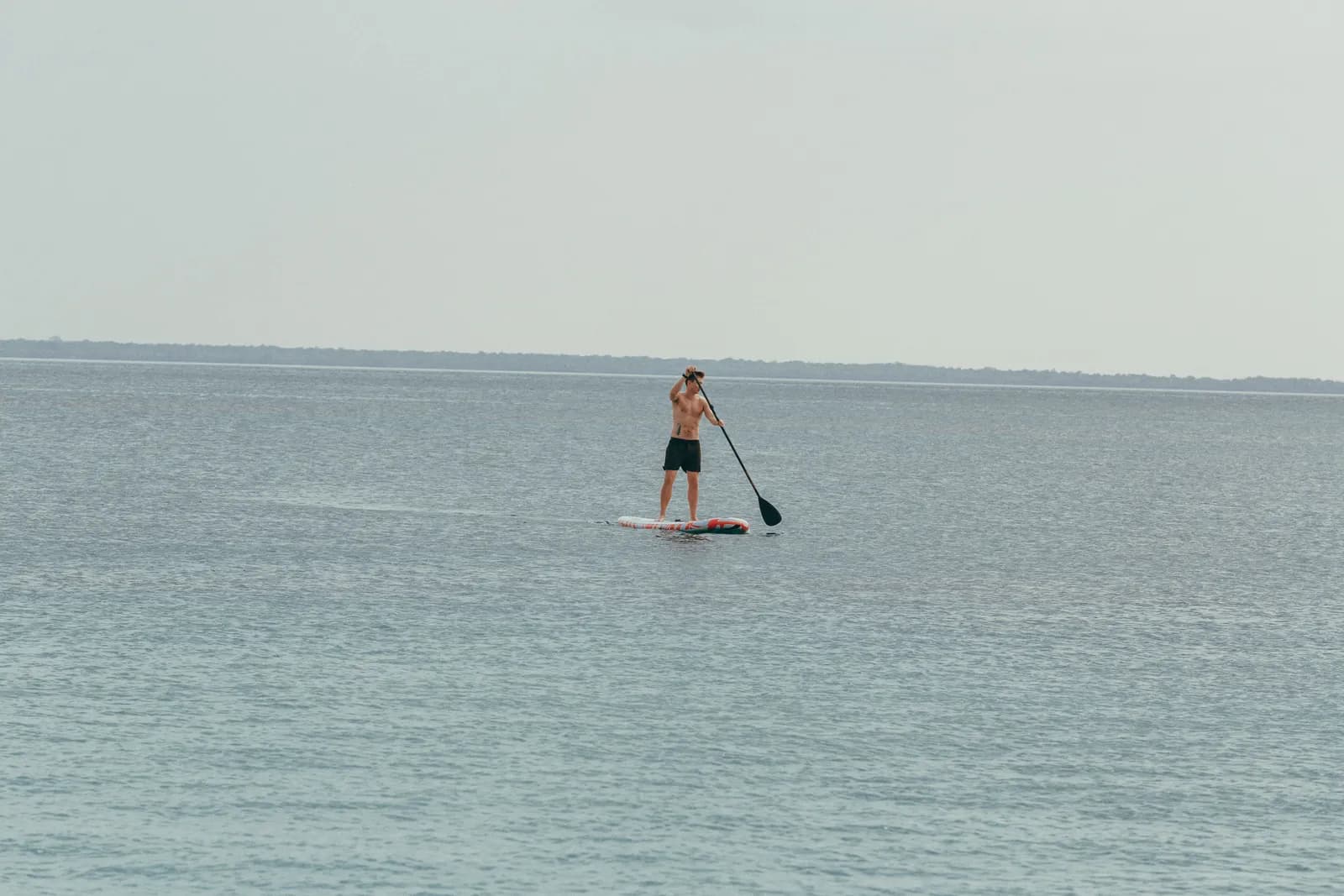 Fit man paddle boarding on calm ocean water during summer vacation for active lifestyle concept