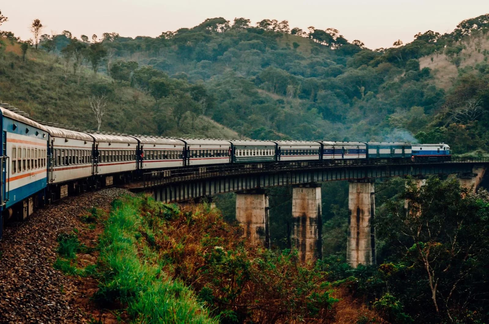 Passenger train traveling on a high bridge through lush green mountains in the countryside landscape