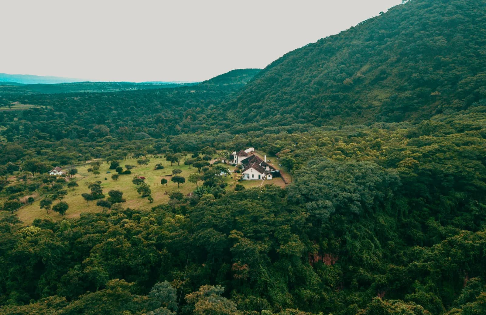 Aerial view of a secluded farmhouse nestled in a lush green valley surrounded by dense forest