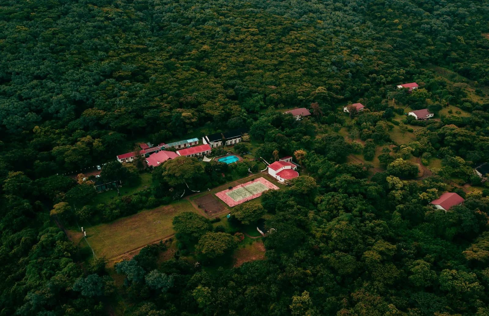 Aerial view of a remote resort complex nestled within a dense green forest with tennis court