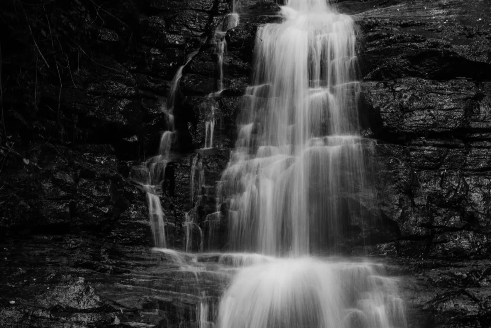 Black and white long exposure of a cascading waterfall flowing over dark textured rock cliffs