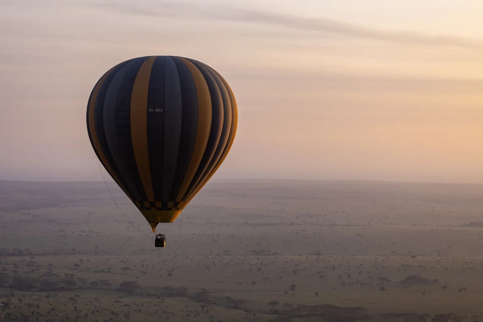 Hot air balloon flying over african savanna landscape during a peaceful sunrise morning flight